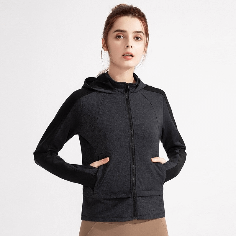Woman wearing black hooded sweatshirt with zipper and thumb holes, ideal for workouts, made from stretchy and quick-drying fabric.